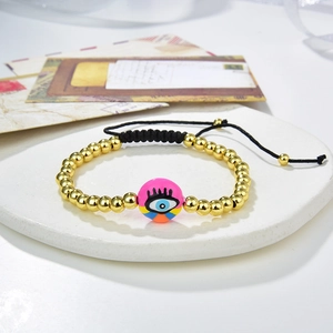 Macro shot of gold copper beads and pink evil eye enamel charm on black woven cord