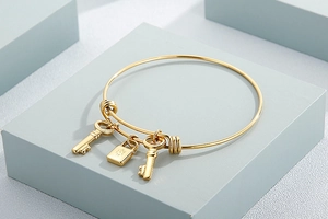 Detailed close-up of golden stainless steel bangle with lock and key charms on blue background