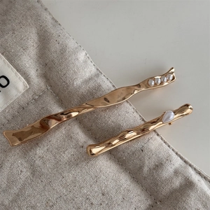 Detail of two wavy gold metal hair clips with pearls on a beige linen pouch