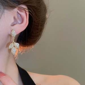 Detail view of leaf-shaped gold drop earrings with sparkling zircon on model