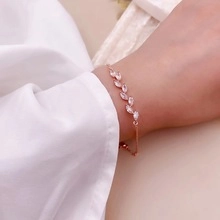 Rose gold bracelet with leaf-shaped gemstones shown on a woman's wrist with soft fabric