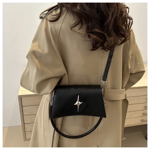Dettaglio di una borsa a tracolla trapezoidale nera con fibbia a stella argento indossata da una modella