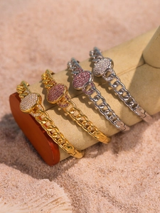 Close-up of gold and silver heart Cuban link bracelets with pink zircons on beach sand