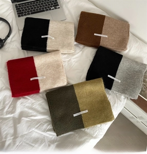 Close-up of five color-block knitted scarves with decorative woven labels on white fabric