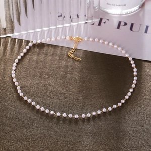 Detailed shot of a delicate 3-4mm pearl necklace with a gold clasp on a brown background