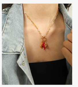 Detail of gold paperclip chain necklace with red chili, heart, and hand gesture charms