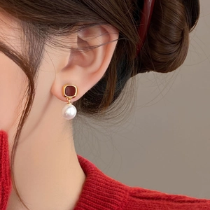 Elegant gold earrings featuring red square stone and pearl drop on a female model