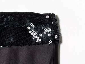 Detailed macro view of black sequin stitching and glossy satin fabric on a tube top