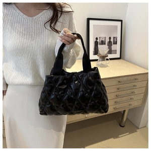 Detail of a black quilted tote bag with a soft puffy texture and stylish wide handle