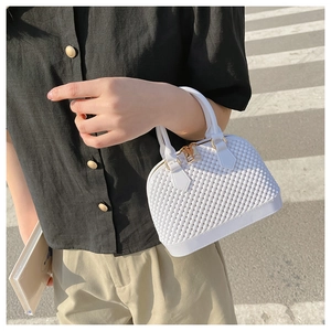 Detail of white quilted jelly bag with gold hardware held by a model on a zebra crossing