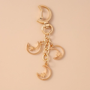 Detail of a golden metal keychain featuring moon and star pendants on a beige backdrop