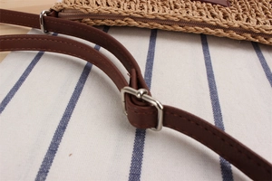 Close-up of khaki woven paper rope bag with brown leather strap and adjustable buckle