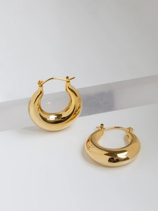 Detailed macro view of polished gold hoop earrings on a modern clear display stand