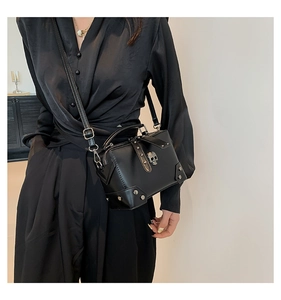 Detailed side view of black crossbody bag with metal skull and silver rivet accents