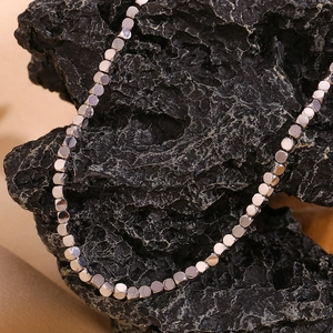 Detail of silver square bead chain necklace draped over a textured black rock