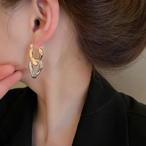 Close-up of gold and silver chunky chain link hoop earrings worn by a model in a black suit