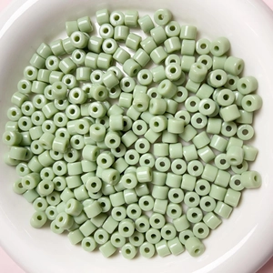 Dettaglio di perle cilindriche in acrilico verde chiaro da 6mm in una ciotola bianca