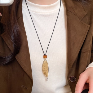Close-up of golden leaf pendant with hammer texture and amber bead on black cord necklace