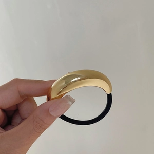 Close-up of polished gold metal arc ornament on a high-elastic black hair tie held in hand