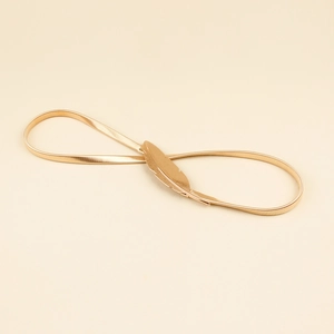 Detailed close-up of golden feather buckle on a metallic stretch belt for women's dresses