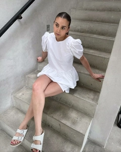 Détail d'une mini robe blanche à manches bouffantes et ourlet volanté sur escalier
