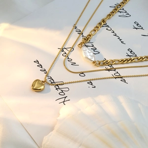 Detailed layered 18k gold heart necklace with pearl charm on white silk background