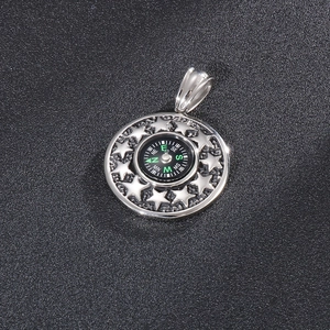 Stainless steel compass pendant with embossed star ring on a textured black surface