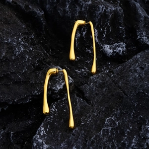 Minimalist gold plated fluid teardrop earrings displayed on a dark textured rock background