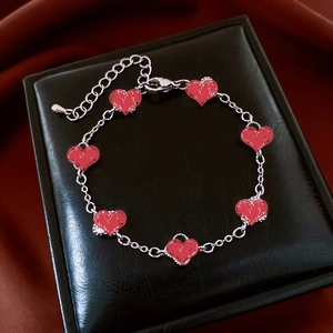 Detail of silver chain bracelet with textured red heart pendants on black leather