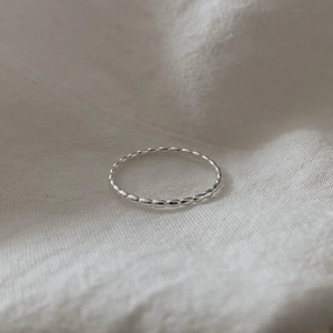 Macro detail of minimalist 925 sterling silver beaded ring on white linen background