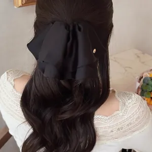 Elegant black satin bow hair claw clip styled on long wavy hair with a golden metal tag