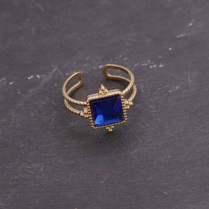 Détail d'une bague dorée vintage avec une pierre carrée bleue et un anneau métallique texturé