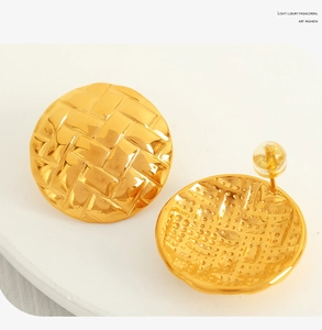 Macro view of gold stainless steel stud earrings with woven texture and clear plastic backings
