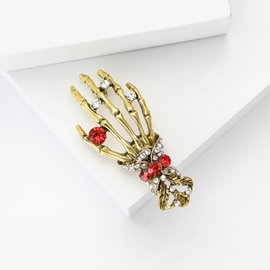 Golden skeleton hand brooch with clear rhinestones and red gems on white background