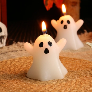 Cute white ghost candles for Halloween decor on a woven mat with warm candlelight