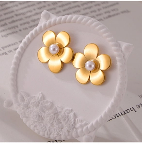 Vue macro de boucles d'oreilles fleur dorée avec perle blanche sur plateau vintage