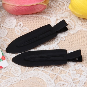 Macro shot of two matte black duckbill hair clips on a delicate beige lace background