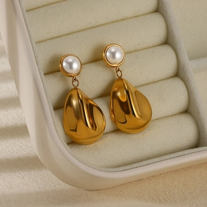 Close-up of golden teardrop earrings with round pearls in a minimalist jewelry box