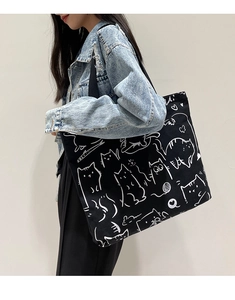 Detail of large canvas tote bag with hand-drawn cat print worn over a denim jacket