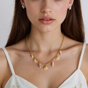 Gold shell necklace with natural seashells and metallic charms on a model with white background