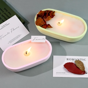 Oval scented candles in green and pink colors with dried flower petals on a grey background