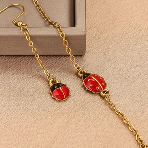 Gold chain jewelry featuring two red ladybug enamel pendants on soft fabric background