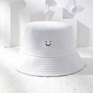 Close-up of white bucket hat featuring black embroidered smiley face and stitched brim