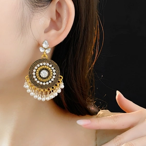 Dettaglio di orecchini vintage dorati con strass scintillanti e nappe di perle bianche