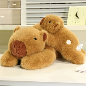 Two soft brown capybara plush pillows in large and small sizes on a desk with warm lighting