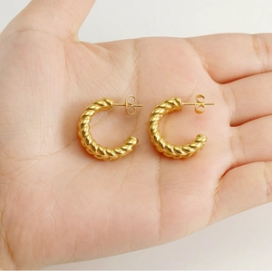 Detail of gold 18k stainless steel twisted C-shape earrings held in a hand
