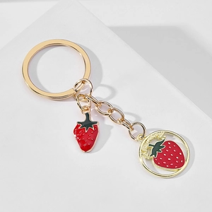 Detail of a golden metal keychain with 3D red strawberry charms and enamel text disc