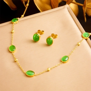 Golden stainless steel jewelry set with oval emerald green stones on silk background