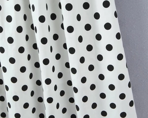 Detailed close-up of white fabric with black polka dots featuring soft drape and texture