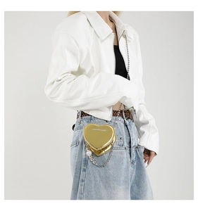 Detail of gold heart-shaped bag with silver chain and white pearl charms on the surface